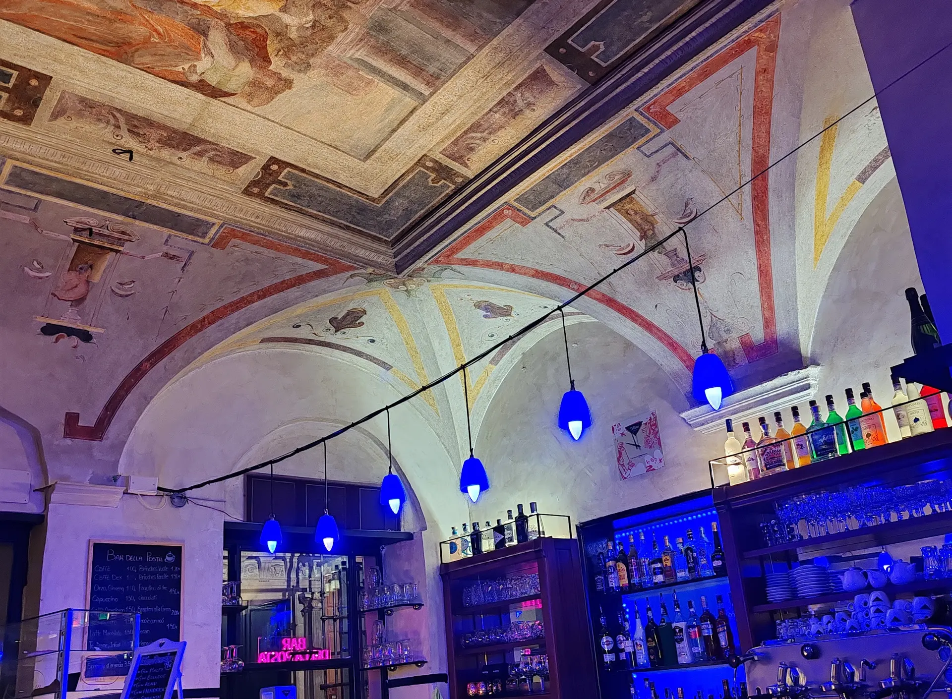 La sala di Posta Vecchia sotto le volte affrescate, con le lampade blu sul bancone